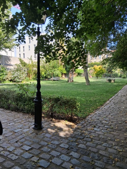 Exuberante jardim do pátio da Villa Raspail em Ivry-sur-Seine com gramado verdejante, árvores maduras e luminária vintage