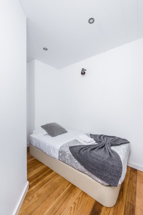 Quarto moderno na Pousada A Lodge in Blue, Aveiro, com cama minimalista, roupa de cama cinzenta e piso em madeira
