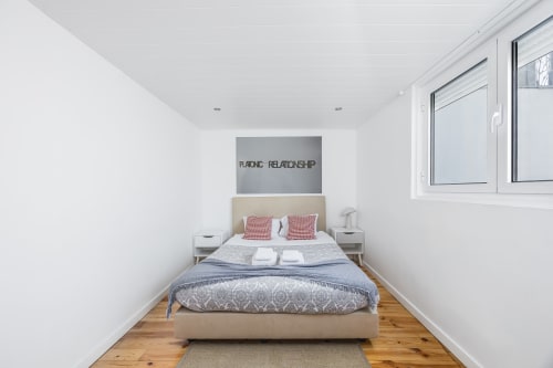 Quarto aconchegante na A Lodge in Blue, Aveiro com cama bege, almofadas xadrez vermelho e piso de madeira