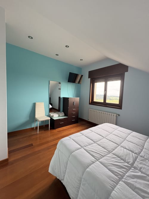 Amplio dormitorio en Casa Aida con pared de acento turquesa, pisos de madera, ropa de cama blanca, muebles de madera oscura y vistas al mar