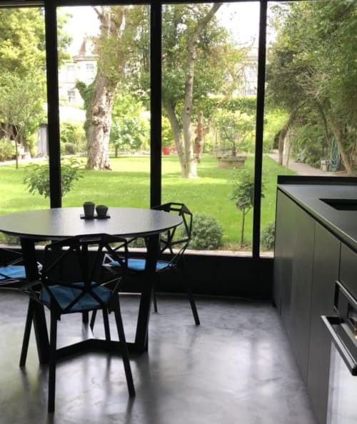Elegante comedor moderno en Villa Raspail con mesa redonda negra, sillas negras y grandes ventanales que se abren a la exuberante naturaleza