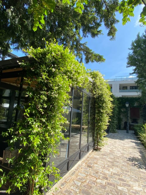 Entrada de pérgola exuberante cubierta de hiedra verde del apartamento-jardín Villa Raspail en Ivry-sur-Seine con puertas de cristal modernas