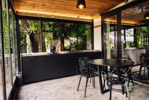 Patio moderno de la Villa Raspail con barra negra, mesa de comedor y vistas al exuberante jardín en Ivry-sur-Seine
