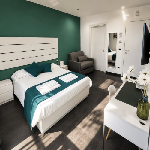 Camera moderna a Soave Rooms B&B Napoli con parete verde foresta, letto bianco con runner turchese e design contemporaneo