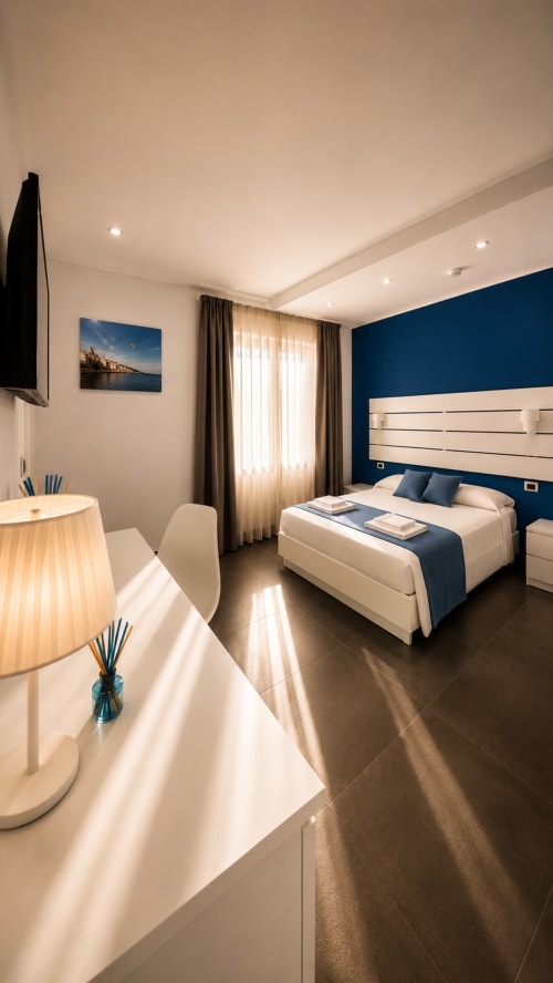 Camera moderna a Soave Rooms a Napoli con parete blu accento, biancheria bianca e arredi contemporanei