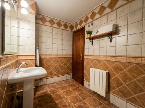 Spacious bathroom at Hospedería Puerta a los Cahorros with tiled walls, pedestal sink, and modern amenities in Monachil