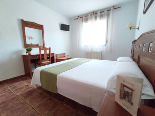Bright hotel room at Hospedería Puerta a los Cahorros in Monachil with twin beds, wooden vanity, TV, and mountain views