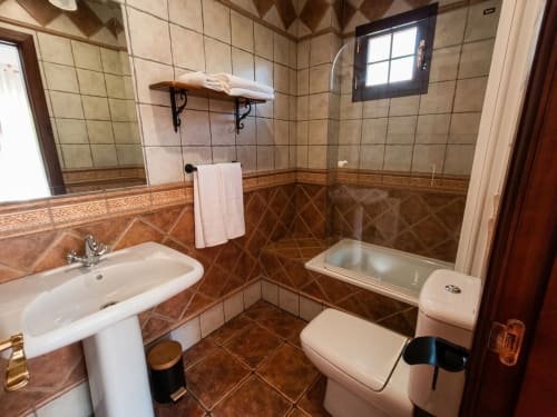 Baño espacioso con paredes alicatadas, lavamanos, inodoro y bañera con cabina de cristal en Hospedería Puerta a los Cahorros