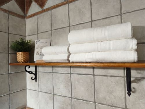 Wooden bathroom shelf with stacked white towels and small potted plant at Hospedería Puerta a los Cahorros, Monachil