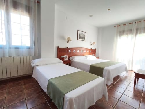 Amplia habitación triple con dos camas, cabecero de madera y acceso a balcón en Hospedería Puerta a los Cahorros, Monachil