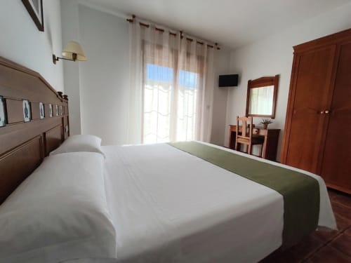 Spacious triple bedroom at Hospedería Puerta a los Cahorros with wooden furniture, balcony access, and river views in