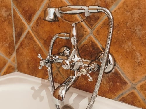 Chrome vintage-style bath faucet with hand shower against terracotta tile wall at Hospedería Puerta a los Cahorros