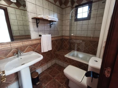 Modern bathroom at Hospedería Puerta a los Cahorros in Monachil with sink, toilet, bathtub and shower area