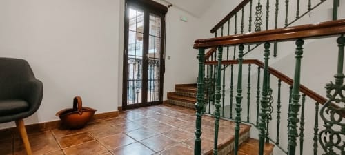 Entrada moderna de hostal con piso de azulejos, barandillas verdes, detalles de madera y puertas de cristal en Hospedería Puerta a los