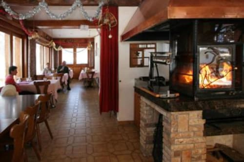 Salle à manger chaleureuse de l'hôtel Les Bouquetins à Anniviers avec cheminée, décor festif et clients dégustant leurs repas