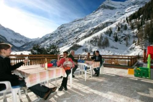 Clients dînant sur la terrasse ensoleillée de l'Hôtel les Bouquetins à Anniviers avec montagnes enneigées