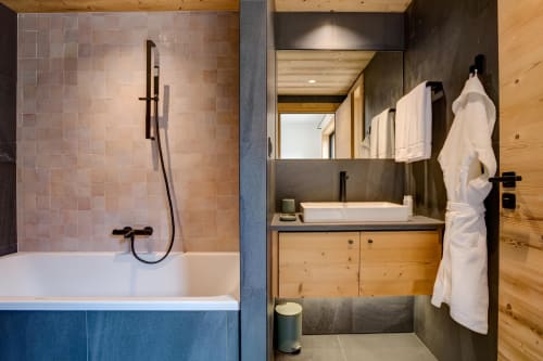 Salle de bain moderne au Chalet Mont-Blanc avec baignoire, vasque, détails en carrelage sombre, meuble bois et serviettes blanches
