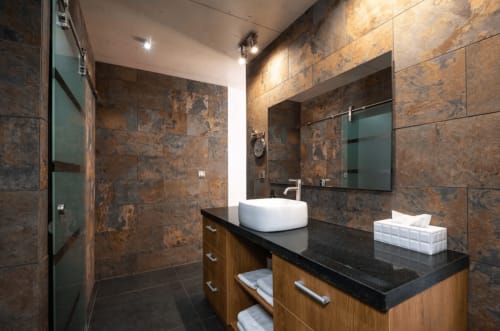 Modern bathroom at Villa Annette in Cassis with bronze tiled walls, vessel sink, black countertop, and wooden vanity.