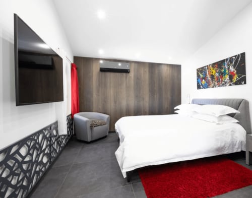 Modern spa bedroom at Villa Annette in Cassis with queen bed, flat-screen TV, gray armchair, and red accent rug.