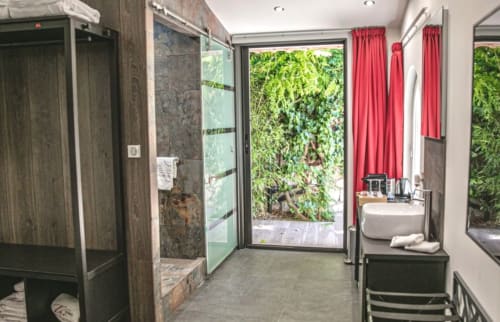 Modern spa bathroom at Villa Annette Cassis with walk-in shower, sink, red curtains, and garden views through glass door