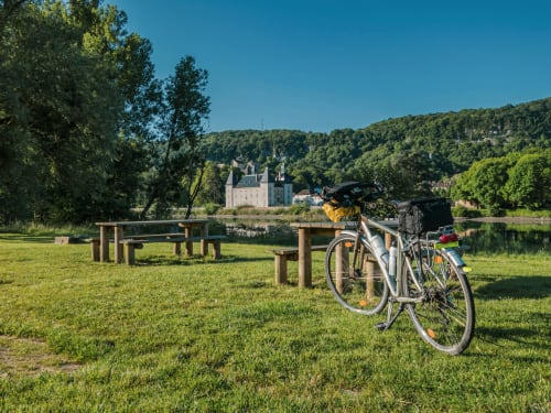 Vélo aux accents jaunes garé sur la pelouse verte du Château Haute Roche à Oudon, France, dominant la rivière et le château.