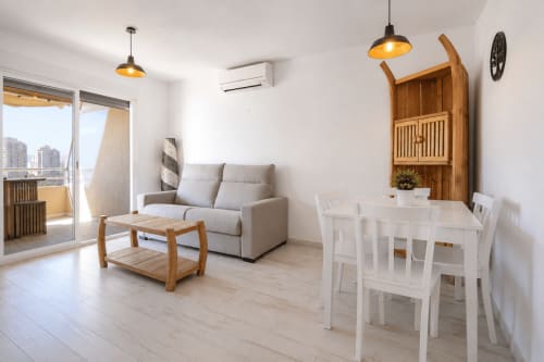 Salón moderno en Calpe con vistas al mar, muebles de madera, mesa blanca y acceso a balcón en Riurau Home