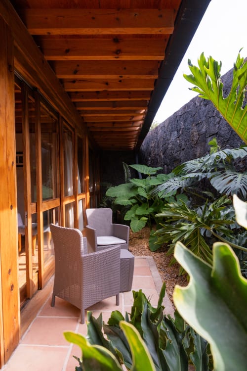 Covered wooden terrace at La Hacienda Tepoztlán with rattan chairs and lush garden plants