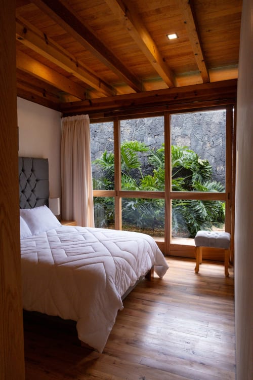 Luxurious bedroom at La Hacienda Tepoztlan with wooden beams, white bedding, and garden views through large windows
