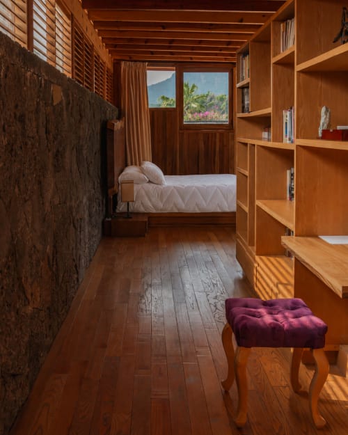 Warm wooden Master Suite at La Hacienda Tepoztlán with mountain views, bookshelf, bed, and purple stool