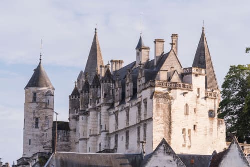Le Perroquet Bleu castle hotel in France with stone towers and turrets against a cloudy sky