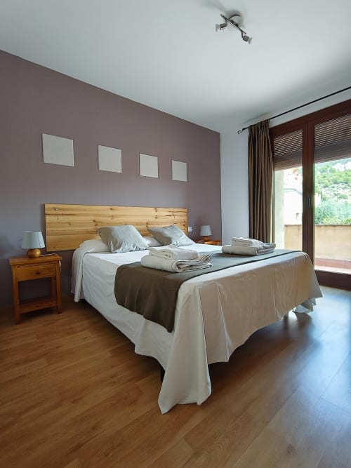 Dormitorio moderno en El Balco del Priorat con cama de madera, paredes malva y vistas a las montañas desde el balcón en Tarragona