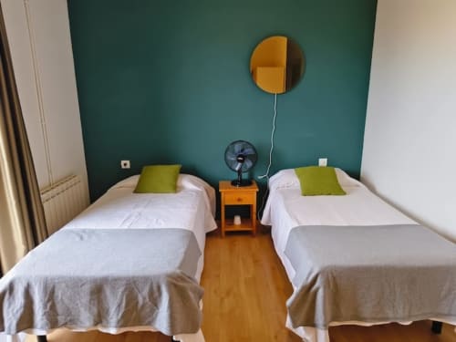 Habitación doble del hotel El Balco del Priorat en Tarragona con pared verde, sábanas blancas y cojines lima