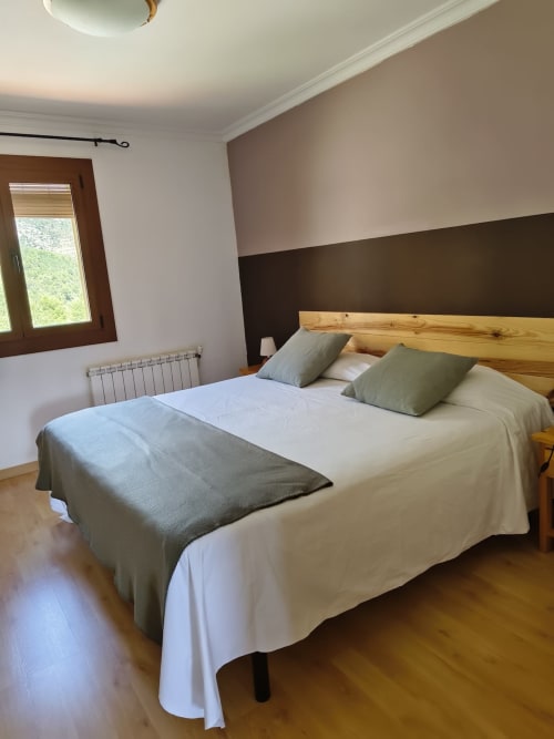 Habitación doble moderna en el hotel El Balco del Priorat de Tarragona con cama de madera, ropa de cama neutra y vistas a las montañas