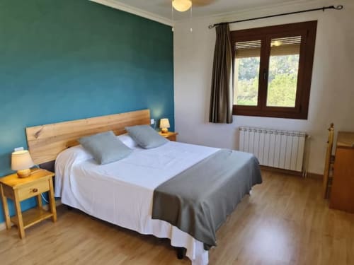 Habitación en esquina del hotel El Balco del Priorat en Tarragona con pared azul, cama de madera y vistas a las montañas