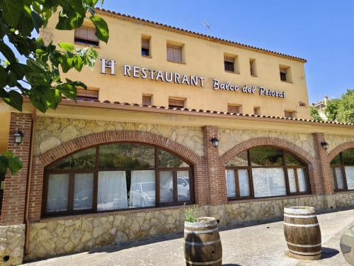 Fachada del restaurante El Balco del Priorat en Tarragona con arcos de piedra, barriles en la terraza y exterior amarillo