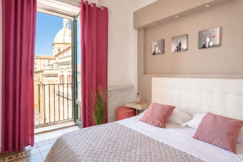 Elegante camera da letto presso I colori della Sicilia a Caltagirone con dettagli rosa, biancheria bianca e balcone con vista sulla cupola.