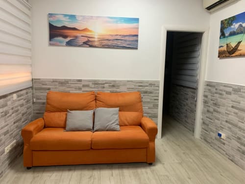 Sofá naranja con cojines grises en salón moderno de apartamento en Benidorm, decorado con cuadro de puesta de sol marina