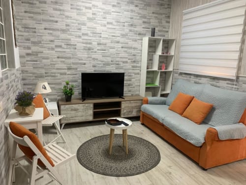 Elegante salón moderno en apartamento de lujo Milan Soria, Benidorm, con sofá naranja, TV de pantalla plana y baldosas grises contemporáneas