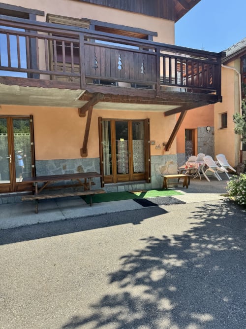 Terrasse ensoleillée aux Chalets La Caillaude à La Salle-les-Alpes avec terrasse en bois, chaises longues et bâtiment orange