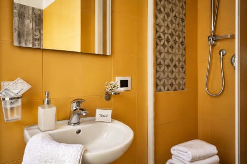 Modern bathroom with golden yellow tiles, white sink, chrome fixtures, and shower at I colori della Sicilia in Caltagirone