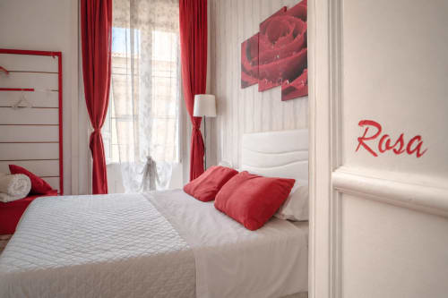 Stanza Rosa presso I colori della Sicilia a Caltagirone: elegante camera con letto matrimoniale, raffinati arredi rossi e bianchi, tende rosse e opere d'arte floreale