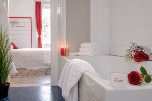 Elegant white bathroom with soaking tub, red roses, and candles at Rosa room in I colori della Sicilia, Caltagirone