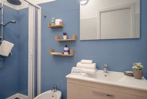 Modern bathroom in Lavanda room at I colori della Sicilia B&B, Caltagirone, featuring blue tile walls, wooden shelves, and