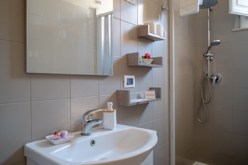 Modern bathroom in Orchidea room at I colori della Sicilia with white sink, wooden shelves, and shower in Caltagirone, Sicily