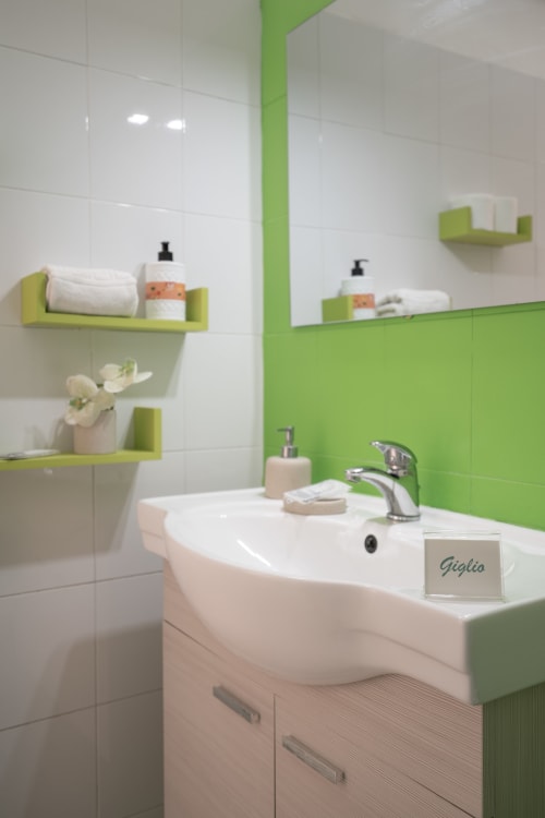 Modern bathroom with green tile accents, white pedestal sink, and lime green shelves at Giglio room, I colori della Sicilia