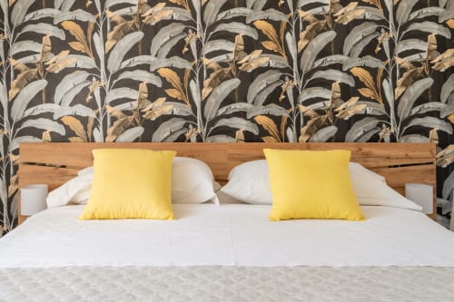 Camera da letto moderna con testata in legno, biancheria bianca, cuscini gialli e carta da parati botanica all'appartamento La Tegola