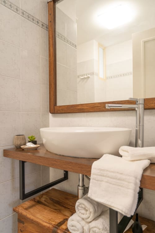 Bagno moderno con lavabo bianco su mobile in legno, specchio con cornice in legno, piastrelle bianche e asciugamani arrotolati presso La Tegola