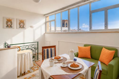Luminoso appartamento a Caltagirone con divano verde, cuscini arancioni, tavolo da pranzo e vista sulla storica torre Campanile