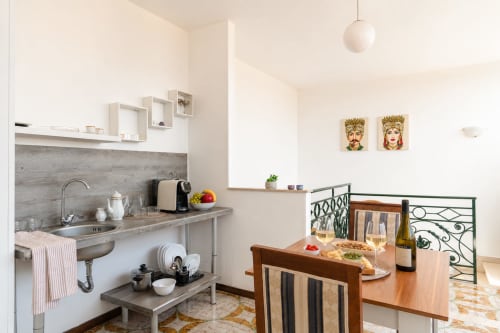 Cucina e zona pranzo di moderno appartamento siciliano con schienale grigio, tavolo preparato con vino e ritratti decorativi