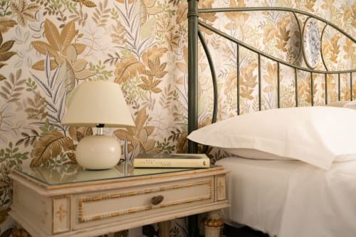 Camera elegante a I colori della Sicilia a Caltagirone con carta da parati floreale, letto in ferro battuto, lampada color crema e comodino.